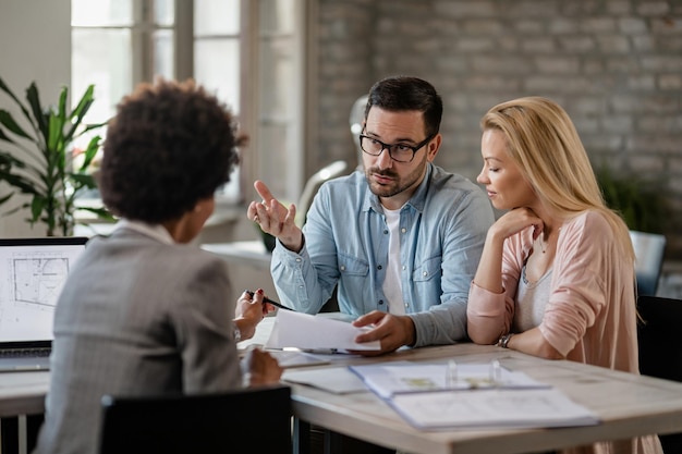 Ein mittleres erwachsenes Paar diskutiert mit einem Finanzberater, während es Dokumente zu einem Meeting im Büro analysiert