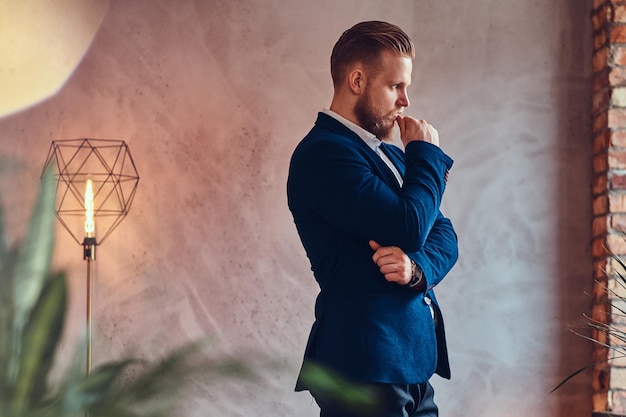 Kostenloses Foto ein moderner, stilvoller mann in einem eleganten anzug, der in einem raum mit loft-interieur posiert.