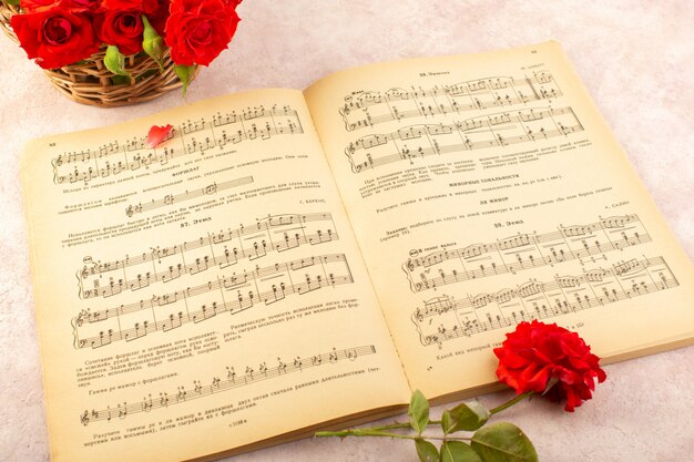 Ein Musiknotenbuch von oben mit geöffneten roten Rosen auf Rosa