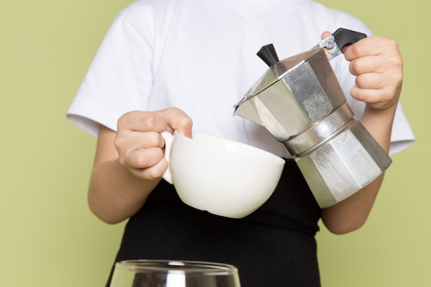 Ein niedlicher Junge der Vorderansicht im weißen T-Shirt, das Kaffeegetränk vorbereitet