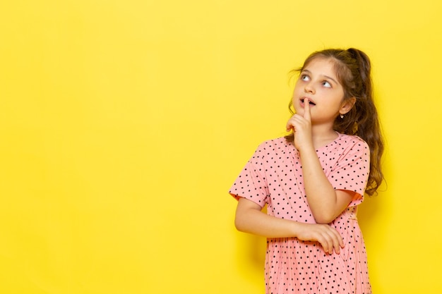 Ein niedliches kleines Kind der Vorderansicht im rosa Kleid, das mit denkendem Ausdruck aufwirft
