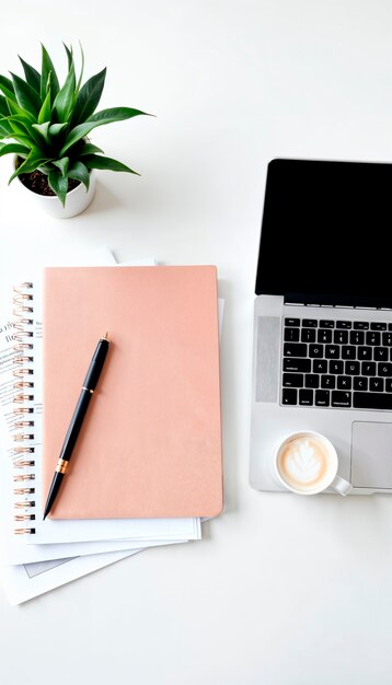 Ein Notizbuch mit einem Stift neben einem Laptop und einer Tasse Kaffee.