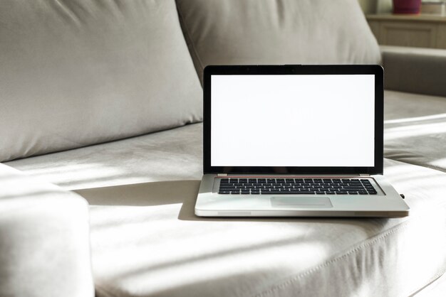 Ein offener Laptop mit weißem Bildschirm auf grauem Sofa