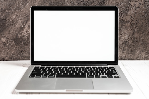 Ein offener moderner Laptop mit einem weißen Bildschirm auf weißem Schreibtisch gegen Betonmauer