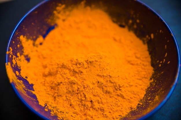 Ein orange Holi-Pulver in der blauen Schüssel gegen schwarzen Hintergrund