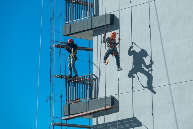 Ein paar Arbeiter, die ein Gerüst reparieren und besteigen, während sie alle Sicherheitsmaßnahmen befolgen