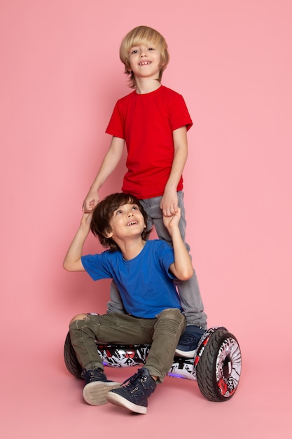 Ein Paar Jungen aus der Vorderansicht in farbigen T-Shirts, die Segway auf dem rosa Raum reiten