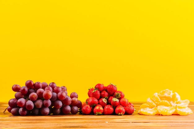 Ein paar Trauben; Erdbeeren und Orangenscheibe auf Holztisch gegen gelben Hintergrund