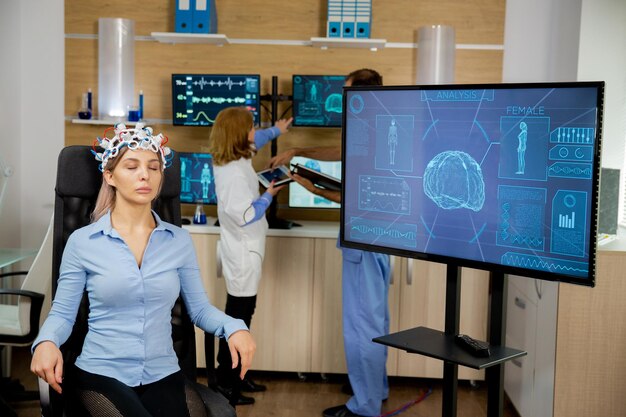 Ein Patient, dessen Gehirn gescannt wird und dessen Aktivität auf dem großen Bildschirm zu sehen ist. Neurologie-Headset