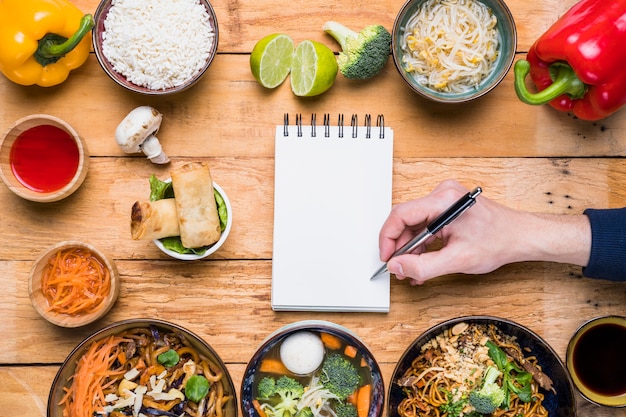 Ein Personenschreiben auf dem Notizblock mit Stift und traditionellem thailändischem Lebensmittel auf Holztisch