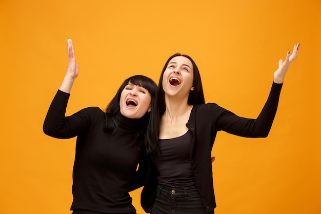 Ein Porträt einer überraschten Mutter und Tochter im Studio auf Goldhintergrund. Trendige Farben. Konzept der menschlichen positiven Emotionen und Gesichtsausdrücke