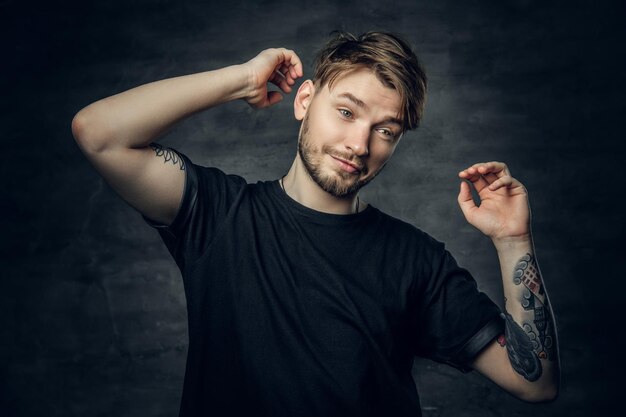 Ein positiver Hipster-Mann in einem schwarzen T-Shirt hält den Kopf mit tätowierten Armen.