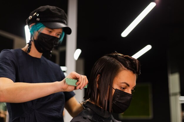 Ein professioneller Friseur macht einen Kundenhaarschnitt. Das Mädchen sitzt in einer Maske in Schönheit im Salon