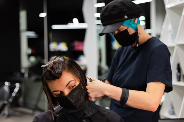 Ein professioneller Friseur macht einen Kundenhaarschnitt. Das Mädchen sitzt in einer Maske in Schönheit im Salon