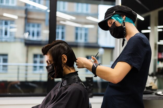 Ein professioneller Friseur macht einen Kundenhaarschnitt. Das Mädchen sitzt in einer Maske in Schönheit im Salon