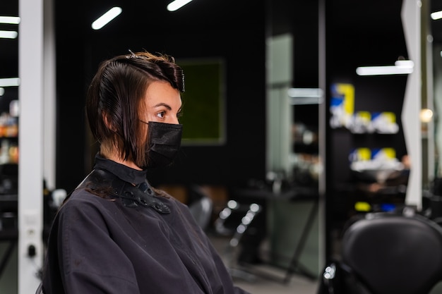 Ein professioneller Friseur macht einen Kundenhaarschnitt. Das Mädchen sitzt in einer Maske in Schönheit im Salon