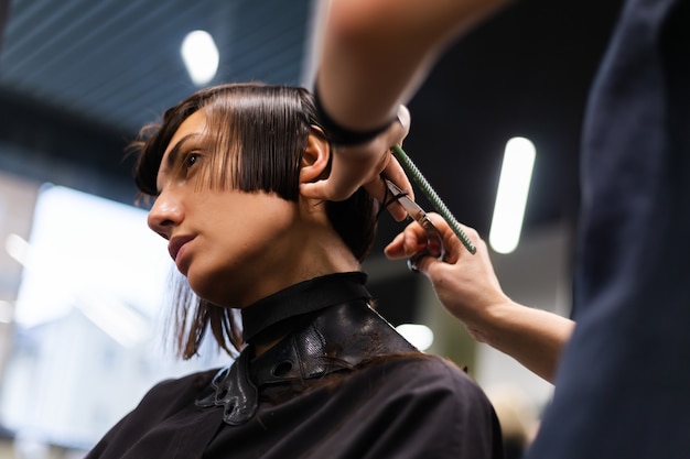 Ein professioneller Friseur macht einen Kundenhaarschnitt. Das Mädchen sitzt in einer Maske in Schönheit im Salon