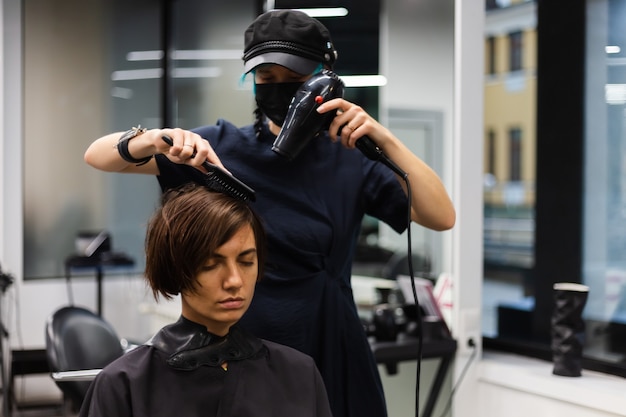 Ein professioneller Friseur macht einen Kundenhaarschnitt. Das Mädchen sitzt in einer Maske in Schönheit im Salon