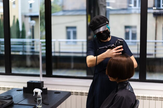 Ein professioneller Friseur macht einen Kundenhaarschnitt. Das Mädchen sitzt in einer Maske in Schönheit im Salon