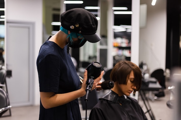 Ein professioneller Friseur macht einen Kundenhaarschnitt. Das Mädchen sitzt in einer Maske in Schönheit im Salon