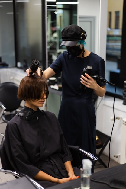 Ein professioneller Friseur macht einen Kundenhaarschnitt. Das Mädchen sitzt in einer Maske in Schönheit im Salon