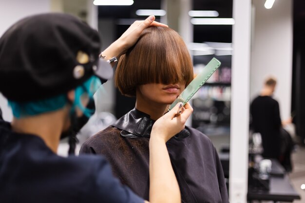 Ein professioneller Friseur macht einen Kundenhaarschnitt. Das Mädchen sitzt in einer Maske in Schönheit im Salon