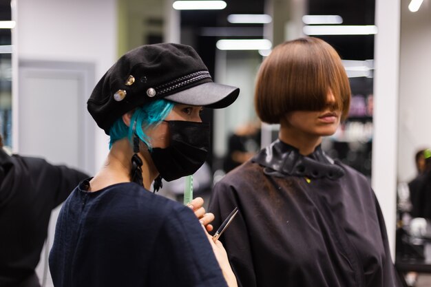 Ein professioneller Friseur macht einen Kundenhaarschnitt. Das Mädchen sitzt in einer Maske in Schönheit im Salon