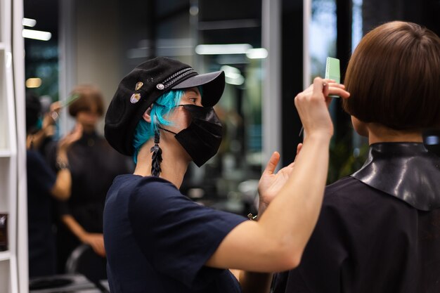 Ein professioneller Friseur macht einen Kundenhaarschnitt. Das Mädchen sitzt in einer Maske in Schönheit im Salon