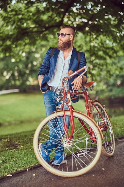 Ein Reisender in Freizeitkleidung und Sonnenbrille mit Rucksack, der sich nach einer Fahrt mit einem Retro-Fahrrad in einem Stadtpark entspannt.