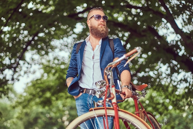 Ein Reisender in Freizeitkleidung und Sonnenbrille mit Rucksack, der sich nach einer Fahrt mit einem Retro-Fahrrad in einem Stadtpark entspannt.