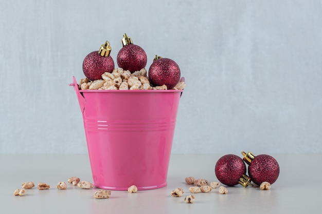 Ein rosa Eimer voller gesundes Getreide mit Weihnachtskugeln.