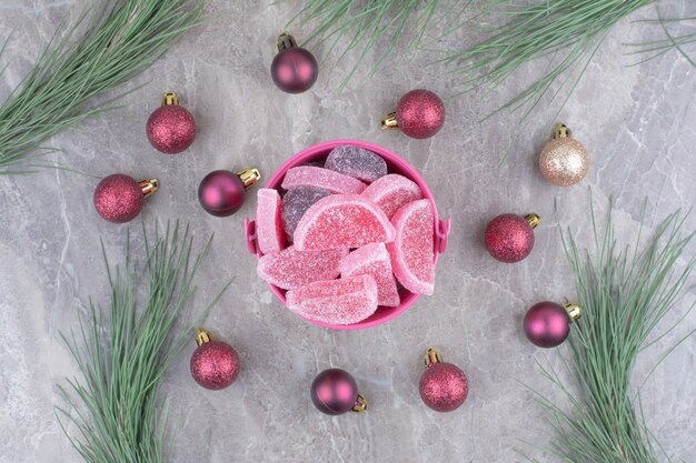 Ein rosa Eimer voller süßer Marmeladen mit roten Weihnachtskugeln auf Marmorhintergrund.