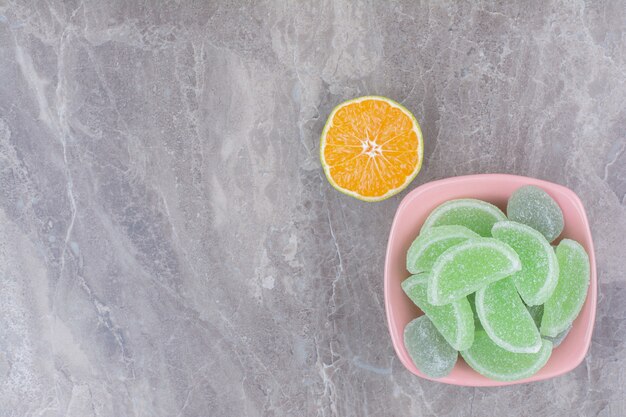 Ein rosa Teller mit Marmeladen und Orangenscheibe auf Marmorhintergrund.