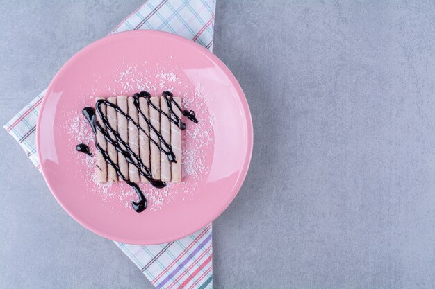 Ein rosa Teller mit süßen Sticks mit Schokoladensirup und Zuckerpulver.