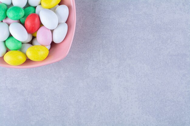 Ein rosa tiefer Teller voller bunter Bohnenbonbons auf grauem Tisch.