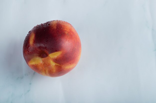 Ein roter Pfirsich auf weißer Oberfläche mit Wassertropfen darauf