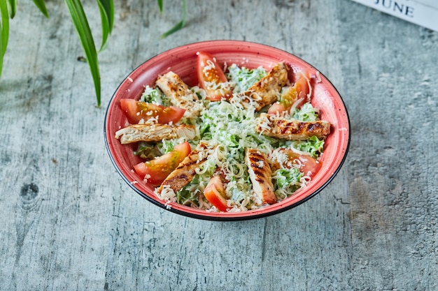 Ein roter Teller mit Caesar-Salat und Tomaten in der Marmoroberfläche