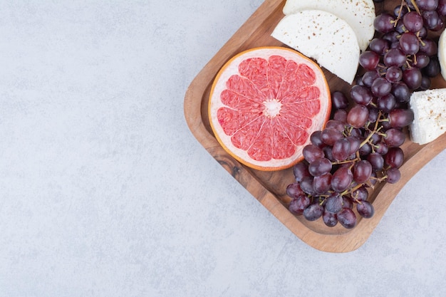 Ein Schneidebrett voller Käse, Grapefruit und Trauben. Foto in hoher Qualität