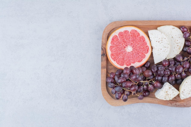 Ein Schneidebrett voller Käse, Grapefruit und Trauben. Foto in hoher Qualität