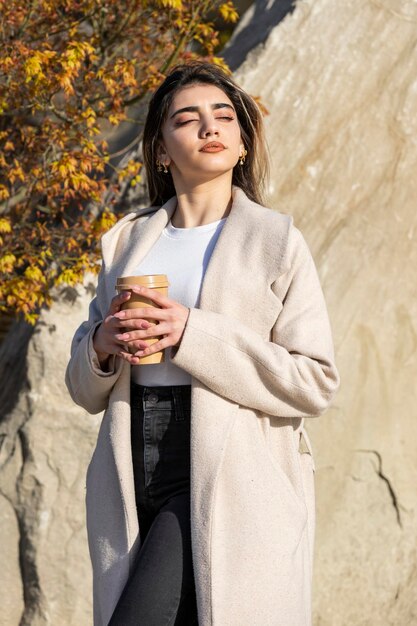 Ein schönes junges Mädchen, das eine Tasse Kaffee hält und die Sonne genießt Hochwertiges Foto