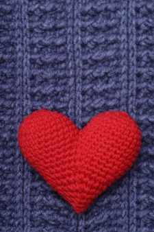 Ein schönes rotes strickherz liegt auf einer blauen strickserviette. liebe konzept. foto in hoher qualität