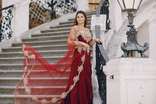 Ein schönes türkisches Mädchen in einem langen roten Kleid geht in die alte Stadt des Sommers