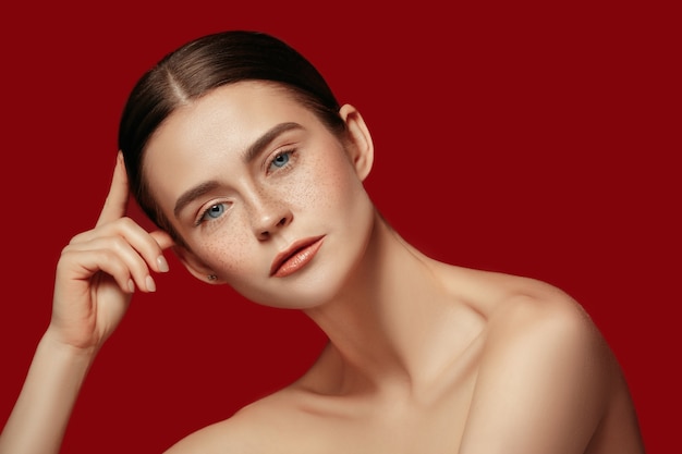 Ein schönes weibliches Gesicht. Perfekte und saubere Haut der jungen kaukasischen Frau auf rotem Studiohintergrund.