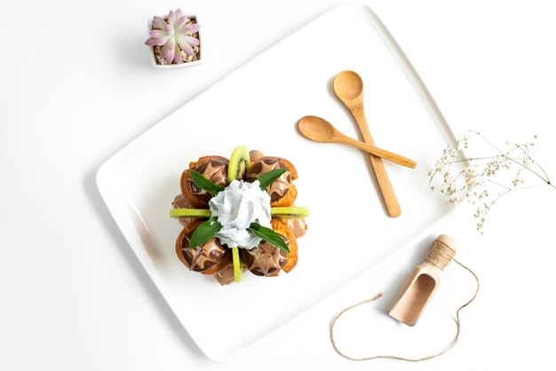 Ein Schoko-Dessert der Draufsicht zusammen mit geschnittenen Kiwis und Vanillepudding innerhalb des weißen Schreibtisches zusammen mit Holzlöffeln auf dem weißen Hintergrundkuchen-Eiscreme süß