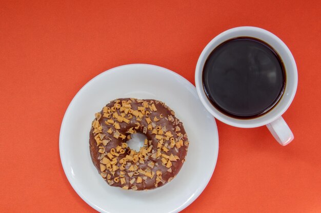 Ein schokoladendonut und schwarzer americano-kaffee ohne milch in einer weißen tasse auf hellem hintergrund. ansicht von oben, flach. frisch gebrühtes oder heißes instant-kaffeegetränk. monochromes konzept.