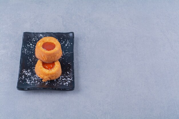 Ein schwarzer Teller mit zwei frischen süßen Cupcakes mit Marmelade.