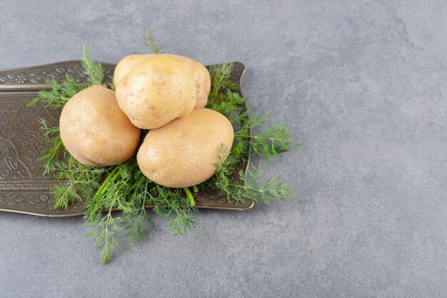 Ein schwarzes Brett mit ungekochten Kartoffeln mit frischem Dill