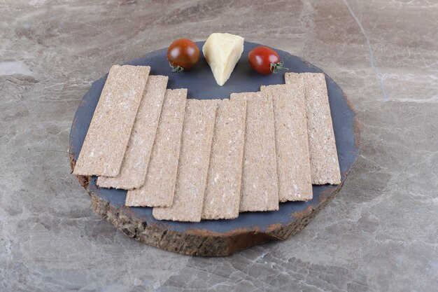 Kostenloses Foto ein stapel knäckebrot, tomaten, käse auf dem holzbrett, auf der marmoroberfläche