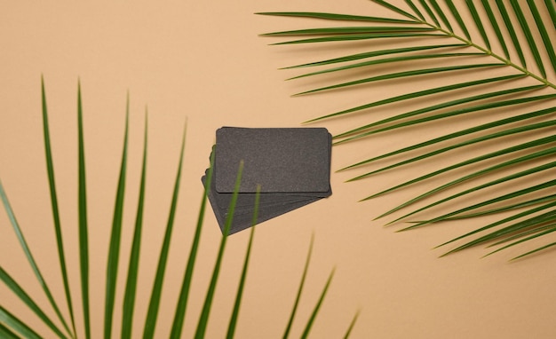 Ein stapel rechteckige visitenkarten aus schwarzem papier und ein blatt einer palme auf braunem hintergrund. sicht von oben