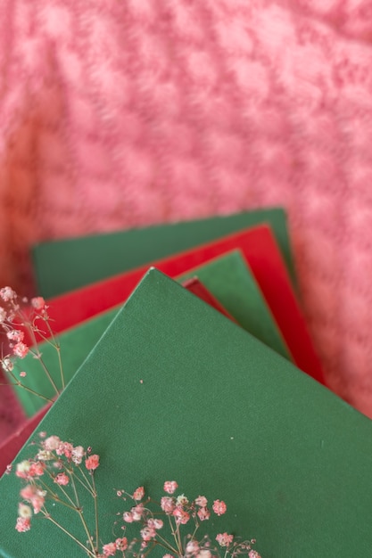 Ein stapel roter und grüner bücher mit trockenen blumen auf einem rosa warmen strickpullover